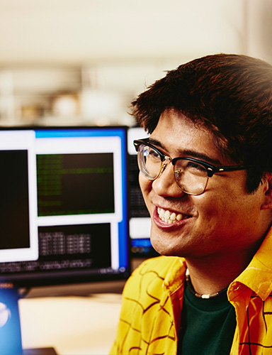 asian male sitting in front of computer smiling and working