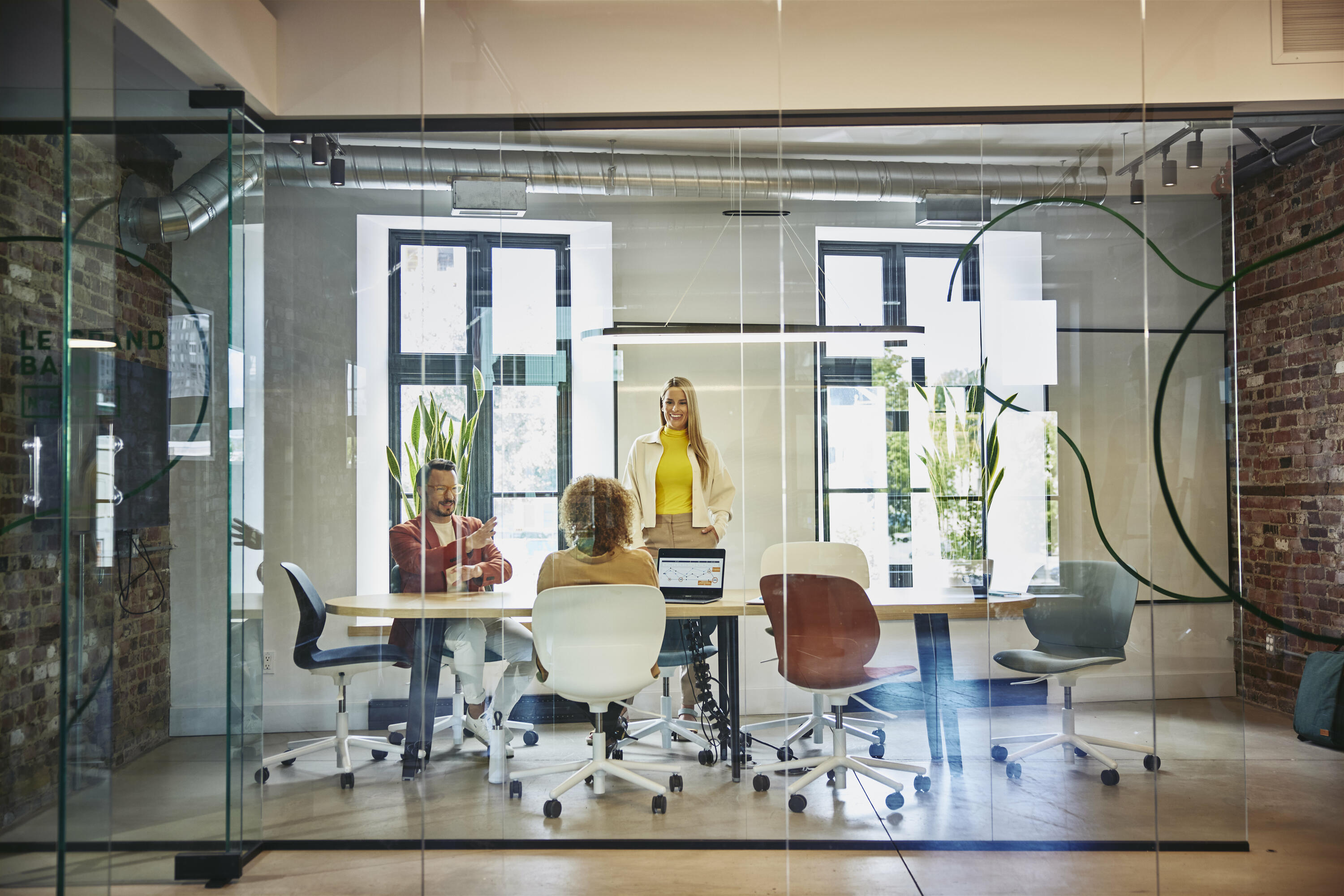 Female and male are sitting and female is standing at a table in a office meeting room