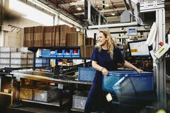 Smiling female standing next to conveyer belt holding a crate

