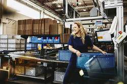 Smiling female standing next to conveyer belt holding a crate
