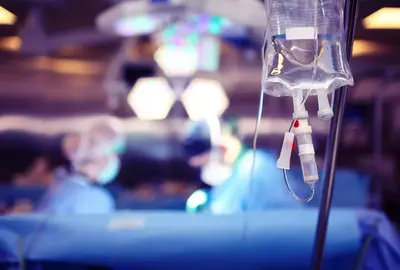Medical dropper hanging on a tripod against the background of a team of surgeons conducting an operation.