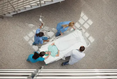 Arial view of nurses and one doctor pushing one patient in a bed in hospital corridor.
