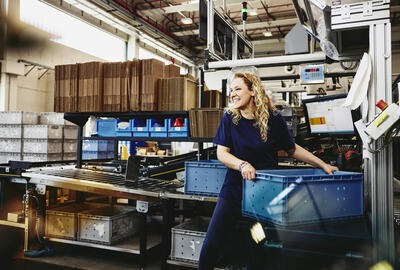 Smiling female standing next to conveyer belt holding a crate
