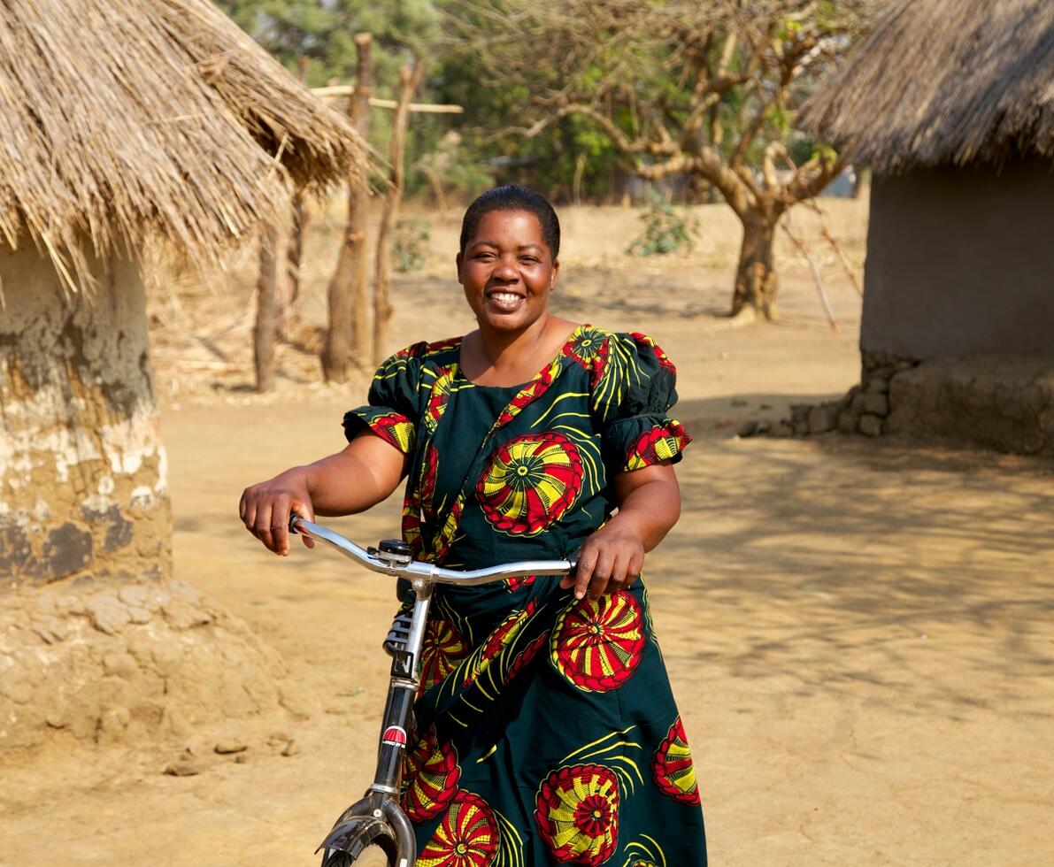 Woman wearing a printed dress holds a bike in an African village