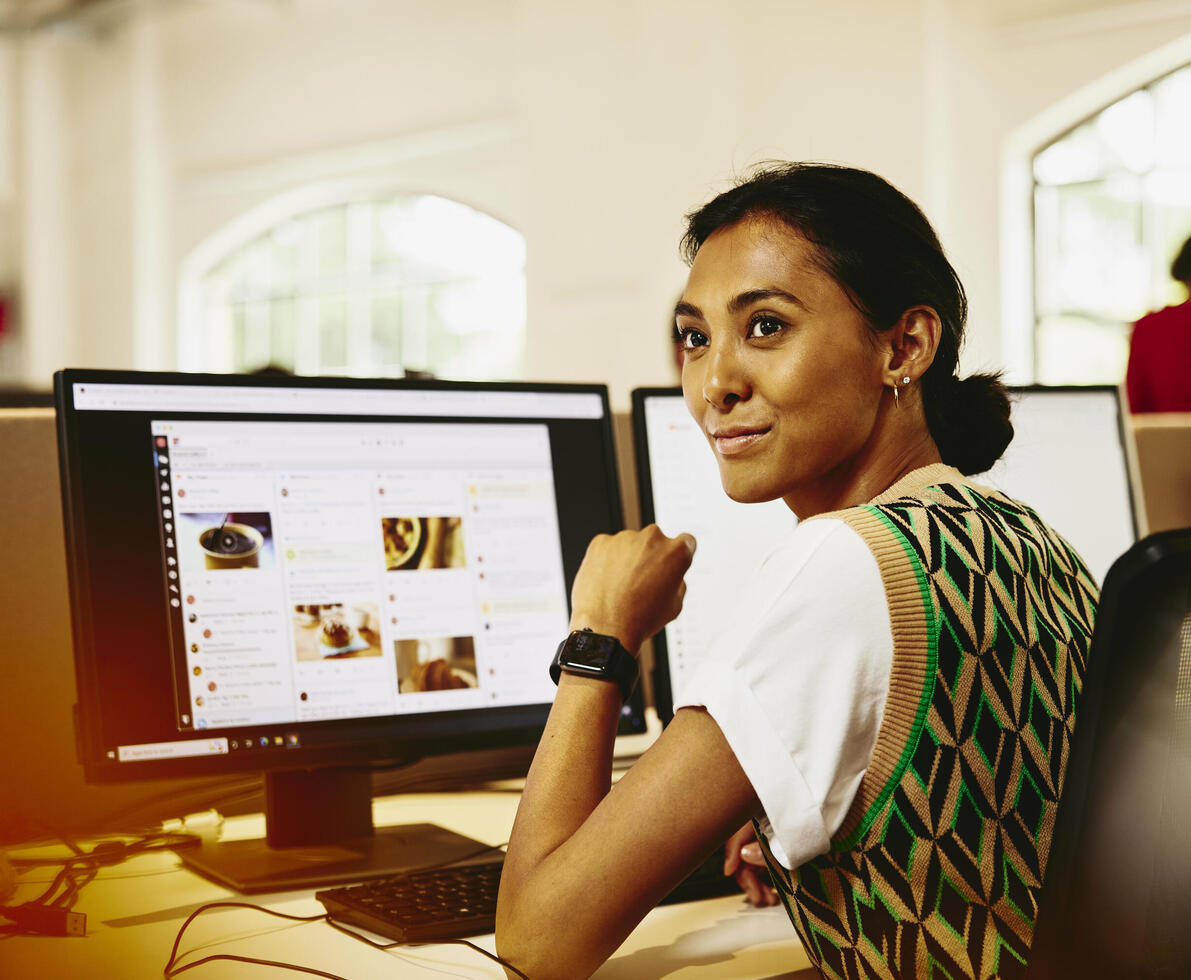 Womale sitting at her desk, looking away from computer screens displaying marketing content.
