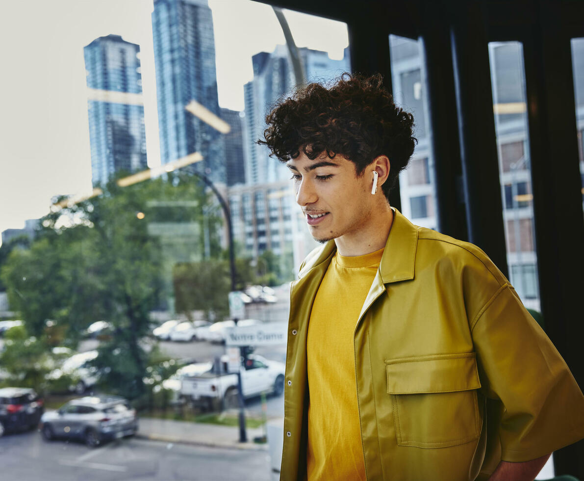 Male in yellow shirt, width earphones, standing at a window looking down