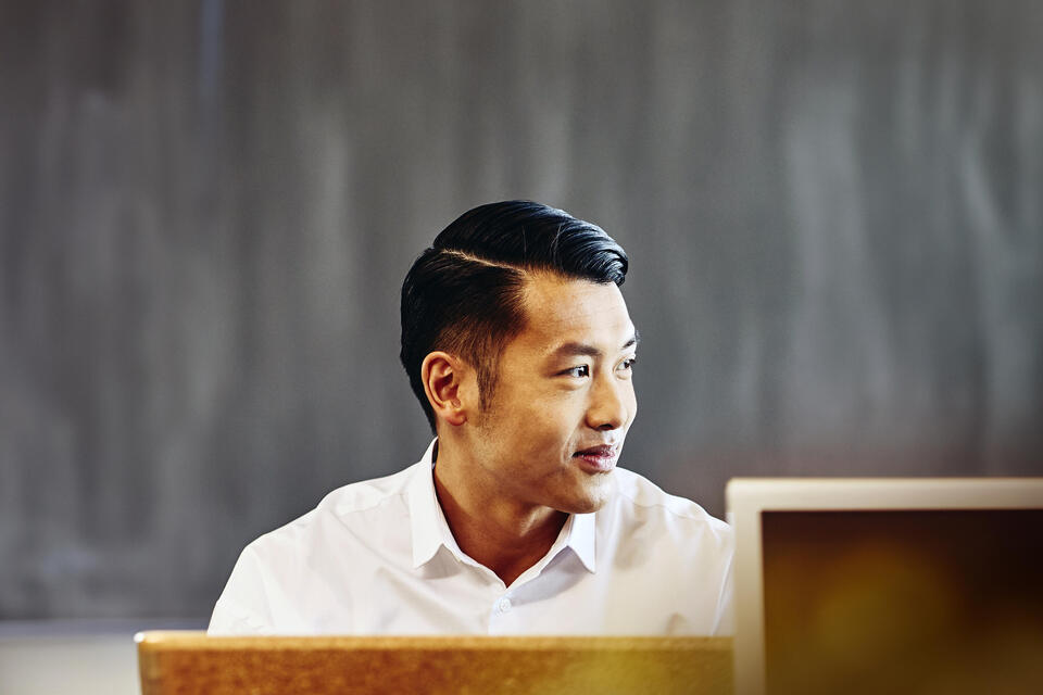 male sitting in an office, smiling and looking away.
