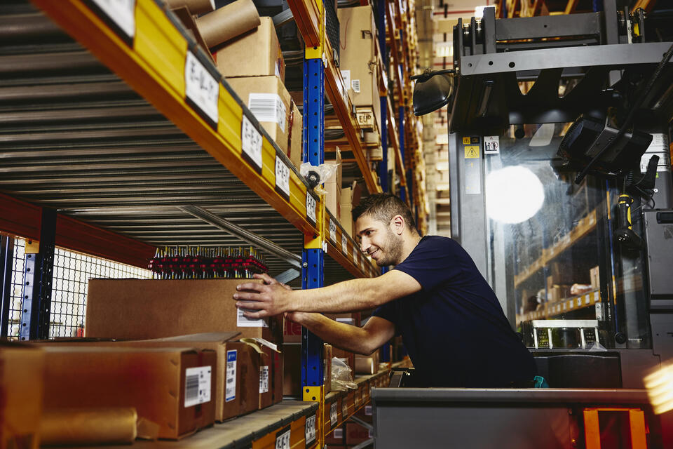 male in elevator between  distribution center racks, picking up a box from a shelf
